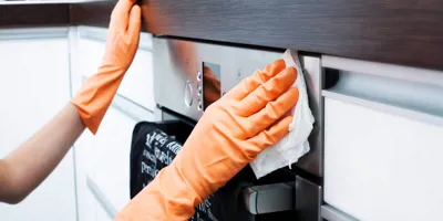 A sütő tisztítása házilag: gumikesztyűs ember papírtörlővel letörli a sütő elejét.