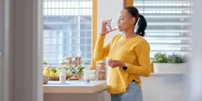 Femeie în pulover galben care bea apă în bucătărie.