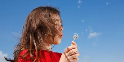 Malo dijete koje će možda trebati kućne lijekove za peludnu groznicu puše u maslačak s plavim nebom u pozadini