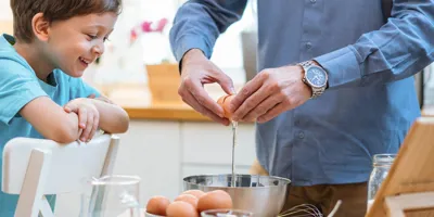 Muškarac i dijete radosno razbijaju jaja u zdjelu za miješanje.