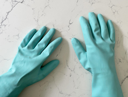 Türkise Haushaltshandschuhe aus dickerem Gummi auf weißem Marmorhintergrund.