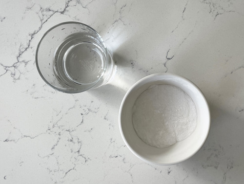 Ein Glas mit Essig und eine weiße Schüssel mit Backpulver/Natron.