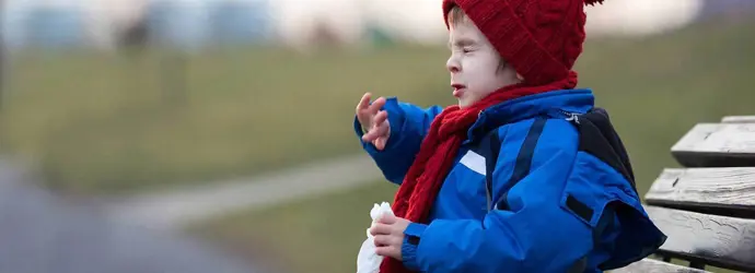 Un copil strănută pe o bancă în parc iarna