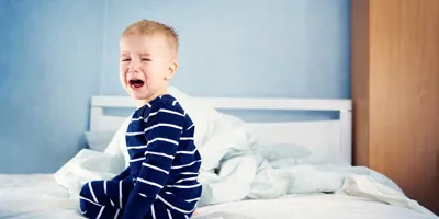 Un copil mic plângând pe un pat nefăcut