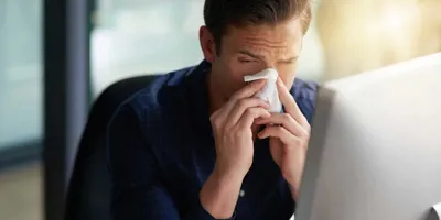 Kýchající muž hledá na počítači inkubační dobu svého nachlazení