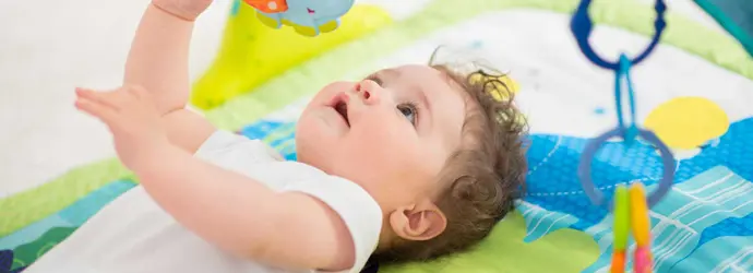 Dítě ležící na barevné podložce a hrající si s hračkami, které mu visí nad hlavou