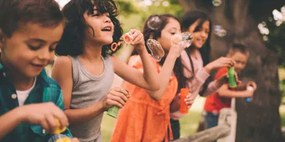 Léto a děti vyfukující bublifuky u dřevěného hrazení