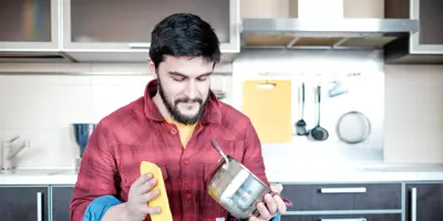 Un bărbat care șterge o oală de aluminiu cu o cârpă într-o bucătărie.