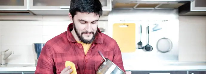 Un bărbat care șterge o oală de aluminiu cu o cârpă într-o bucătărie.