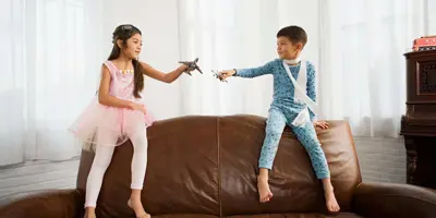 Egy kislány és egy kisfiú egy barna bőr kanapé tetején ülnek, kezükben játék repülőkkel.