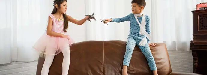 Egy kislány és egy kisfiú egy barna bőr kanapé tetején ülnek, kezükben játék repülőkkel.