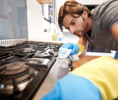 Szürke pólós, gumikesztyűs férfi főzőlapot tisztít puha ronggyal.