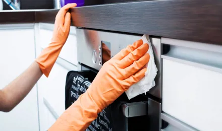 A sütő tisztítása házilag: gumikesztyűs ember papírtörlővel letörli a sütő elejét.