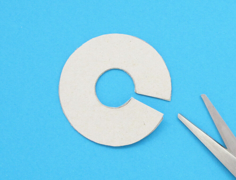 Kartonból készült kivágás vastag gyűrűből, vékony ék alakú kivágással, oldalán ollóval.