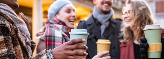 Lachende Freunde halten draußen Kaffeetassen.