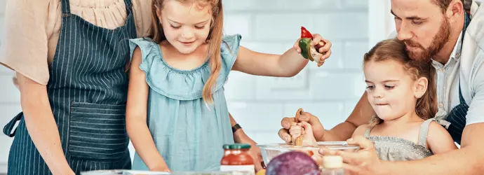 Eine junge Familie mit zwei kleinen Mädchen hat Spaß daran, in der Küche zusammen Essen zuzubereiten.