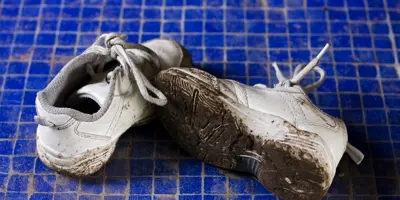 Ein Paar weiße, mit Schlamm verschmutzte Turnschuhe auf einem Untergrund.