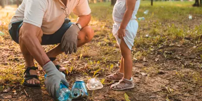 Bunicul îl învață pe un copil mic să strângă gunoiul într-un parc însorit.