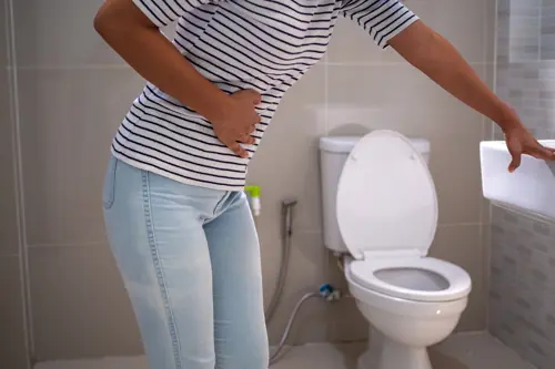Eine Person hält sich den Unterleib, während sie in der Nähe einer Toilette steht.