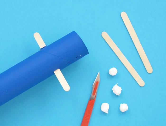 Картонена ролка, пръчки от близалки или сладолед, малки хартиени топчета, макетно ножче.