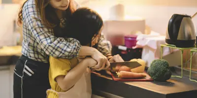 Eine Frau hilft ihrer Tochter, Karotten mit einem scharfen Messer in einer kleinen Küche zu schneiden.