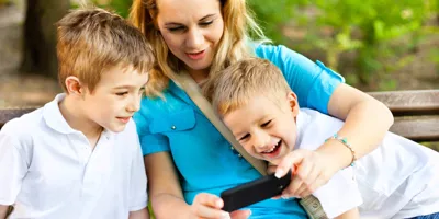 Doi băieți și mama lor se uită la ecranul unui smartphone și zâmbesc. 
