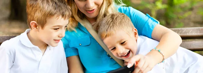 Doi băieți și mama lor se uită la ecranul unui smartphone și zâmbesc.