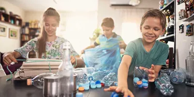 3 παιδιά προσπαθούν να καταλάβουν τι μπορούν να ανακυκλώσουν, βάζοντας διάφορα είδη πλαστικών σε κάδους στην κουζίνα