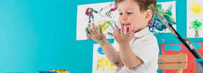 Ein Kind sitzt an einem Tisch und malt mit den Fingern