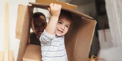 Момченце държи картонена кутия за преместване в ново жилище със семейството си
