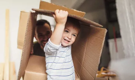 Момченце държи картонена кутия за преместване в ново жилище със семейството си