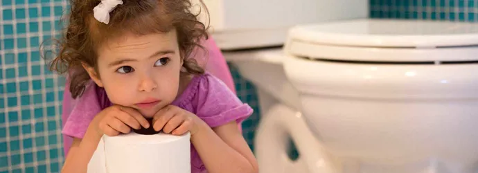 Маленькая девочка сидит на горшке и держит рулон туалетной бумаги в руках