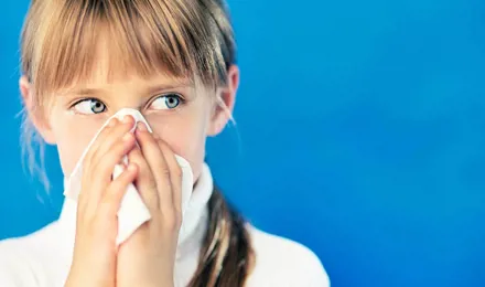 Девочка с простудой держит бумажную салфетку перед носом