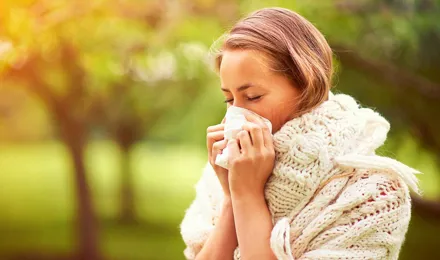 Молодая женщина в джемпере сидит в парке, чихая, и думает о причинах ее сенной лихорадки