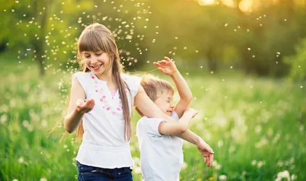 Брат и сестра играют на поле одуванчиков, окруженные пыльцой