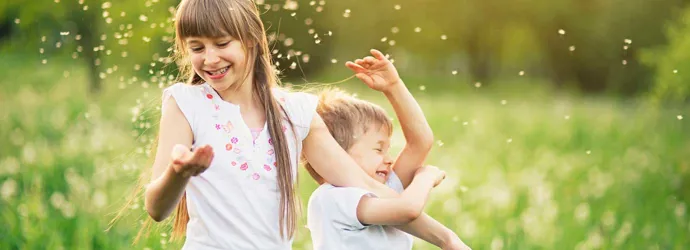 Брат и сестра играют на поле одуванчиков, окруженные пыльцой
