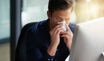 Человек чихает на свой компьютер и ищет инкубационный период при простуде