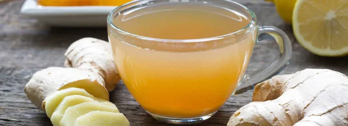 Целый и нарезанный имбирь, мед, лимон, и стакан смеси на деревянном столе