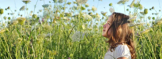 Молодая девушка, которой могут понадобиться средства от сенной лихорадки, стоит в солнечный день в поле с большим количеством высоких, диких цветов