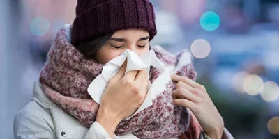 Жінка, загорнута у зимовий одяг, страждає на симптоми синуситу та чхання