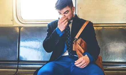 Egy öltönyös férfi ül a vonaton az orrát fújva