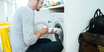 Muškarac stavlja odjeću u perilicu rublja