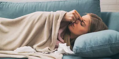 Žena leži na plavom kauču i osjeća da je bole sinusi