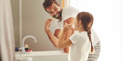 Muž a jeho mladá dcera se učí šetřit vodou při čistění zubů v koupelně