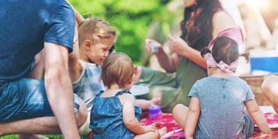 Skupina dospělých a dětí sedící na dece při rodinném pikniku