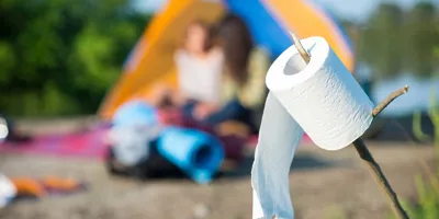 Pisilés a szabadban: WC-papír guriga látható egy boton, a háttérben kültéri játszótér gyerekekkel.  