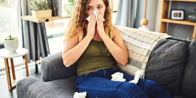 Femeie cu simptome de alergie sau răceală își suflă nasul