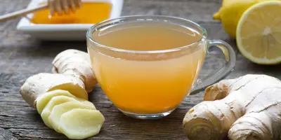 ghimbir întreg și tocat, miere, lămâie și un pahar cu acestea amestecate, toate pe o masă de lemn.