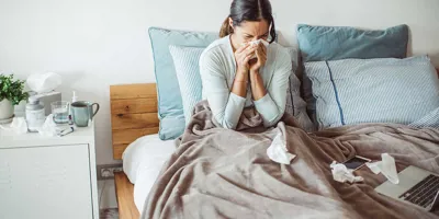 Žena u krevetu puše nos u maramicu
