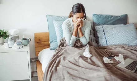 Žena u krevetu puše nos u maramicu
